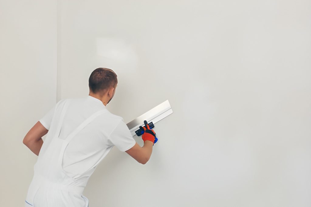 A man worker plasters the wall with a spatula and applies a cement mix solution.